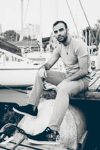 Retrato de hombre sexy sentado en el muelle en el puerto con yates —  Fotos de Stock