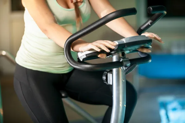 Woman riding exercise bike against swimming pool — Stock Photo, Image