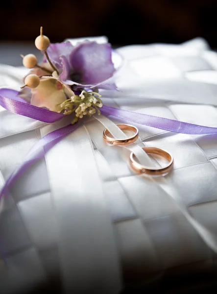 Anillos de boda acostados en cojín de satén decorado con flores — Foto de Stock