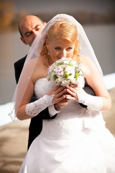 Bräutigam umarmt schöne Braut, die Blumen riecht — Stockfoto