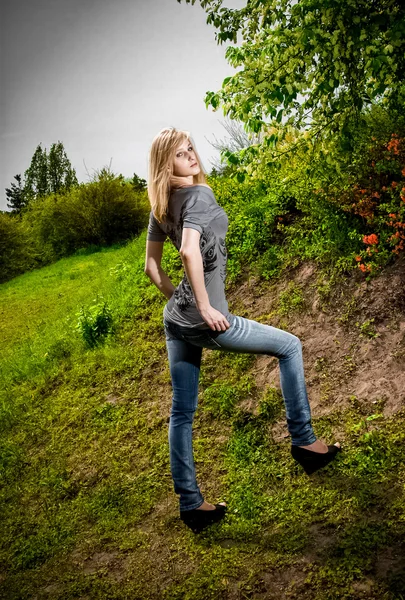 Blondine in Jeans steht auf einem Hügel im Park — Stockfoto