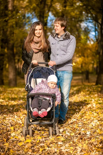 Family walking with pram at autumn park — Stock Photo, Image