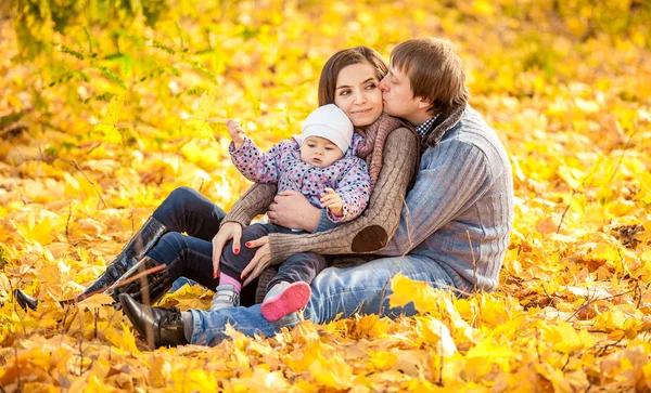 Familjen sitter på blad på hösten park — Stockfoto