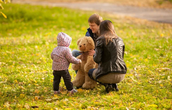 Menina brincando com ursinho de pelúcia e pais no parque — Fotografia de Stock