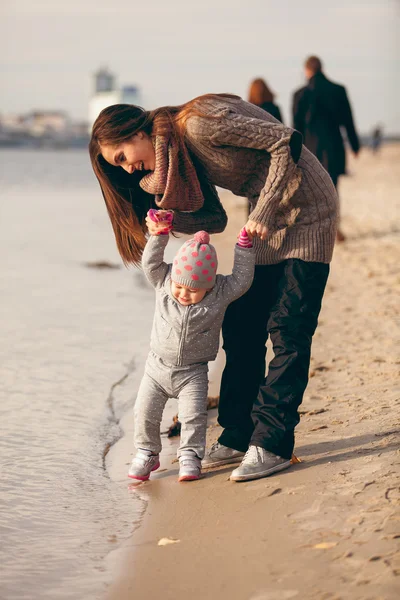 Маленькая девочка делает первые шаги на пляже с помощью — стоковое фото