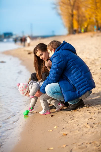 Дочь копает песок с лопатой на пляже с родителями — стоковое фото