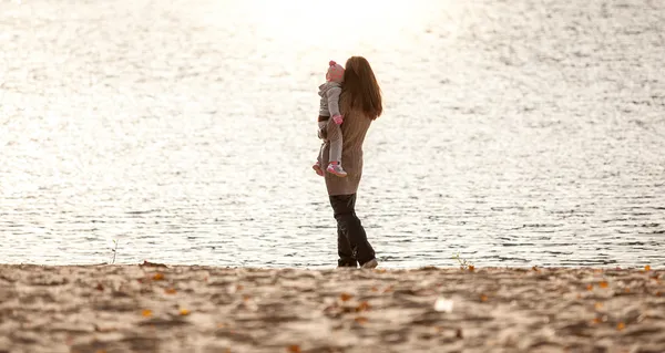 Madre sosteniendo hija en las manos y mirando al mar — Foto de Stock