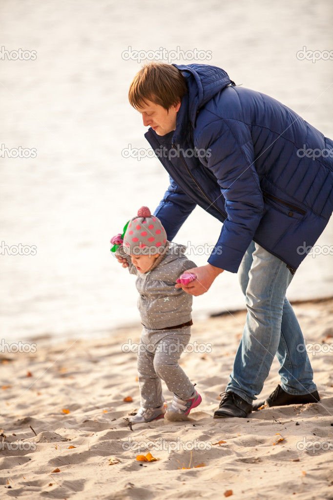father walking with small daughter on beach at autumn