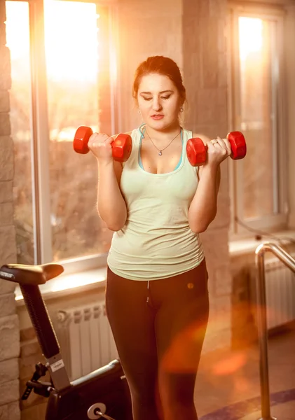 Mujer joven levantando pesas en el gimnasio al atardecer — Foto de Stock