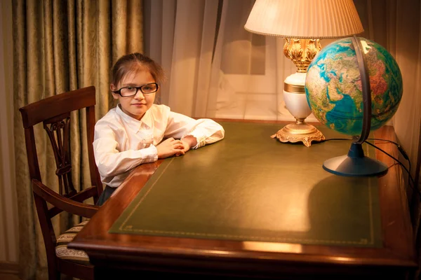 Petite fille aux lunettes assise derrière le bureau — Photo