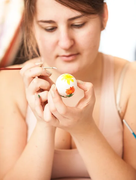 Брюнетка рисует белое пасхальное яйцо — стоковое фото
