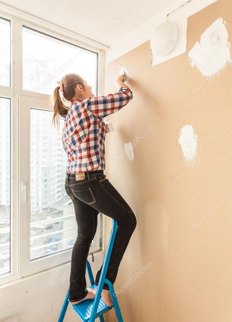 Woman working with putty and spatula on ladder