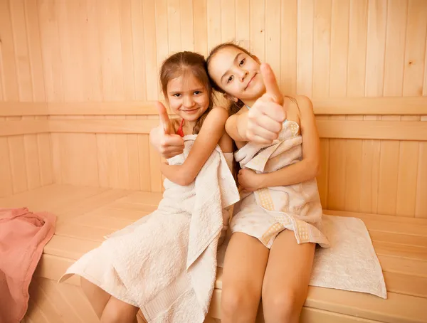 Щасливі маленькі дівчата в сауні показують великі пальці вгору — стокове фото