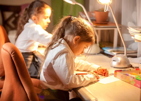 Liten skolflicka sitter bakom tabell och ritning — Stockfoto