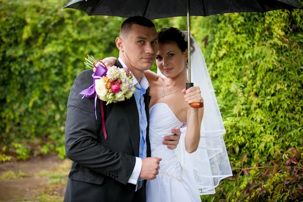 Portrait of happy bride and groom standing under umbrella — Stock Photo, Image