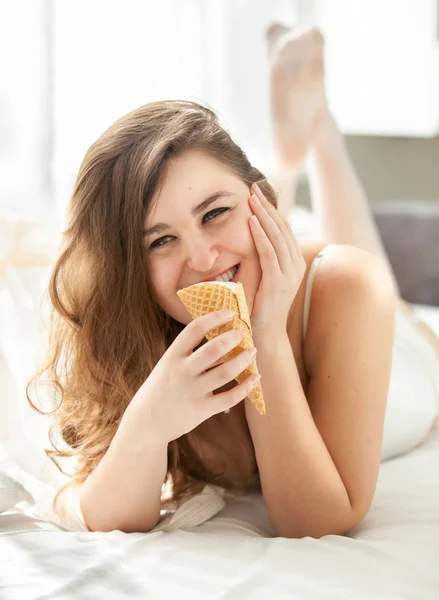 Foto de una mujer sonriente comiendo helado en la cama —  Fotos de Stock