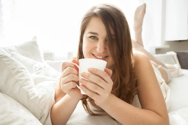 Sonriente mujer bebiendo café en la cama por la mañana —  Fotos de Stock