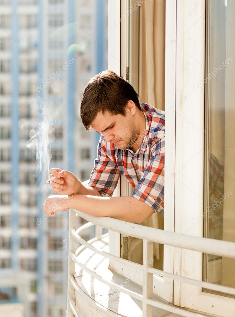 depressed man smoking cigarette out of window