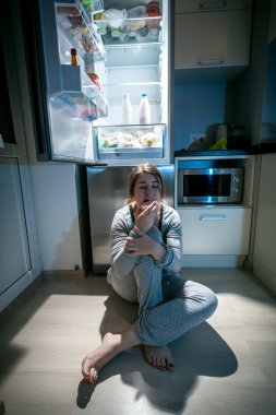 vrouw zitten in de buurt van koelkast in de late nacht
