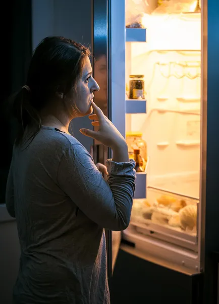 Женщина смотрит в холодильник поздно вечером — стоковое фото