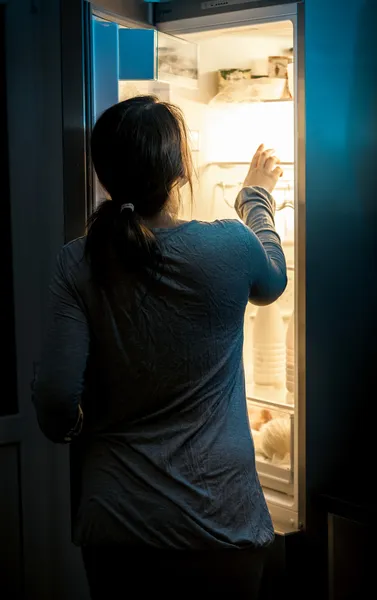 Mujer hambrienta mirando en la nevera en la noche —  Fotos de Stock