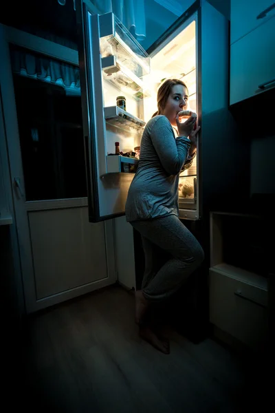 Hungrige Frau isst nachts in der Nähe des Kühlschranks — Stockfoto