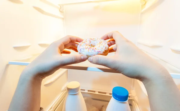 Фото женской руки, берущей пончик из холодильника — стоковое фото
