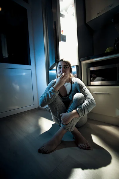 Женщина ест пончики на полу кухни — стоковое фото