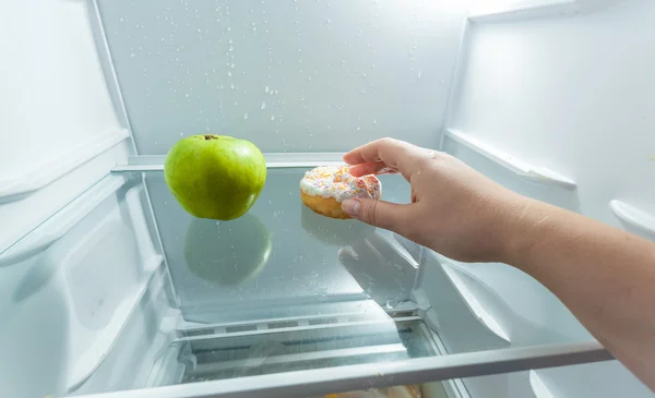 Tangan memilih donat bukan apel tergeletak di lemari es — Stok Foto