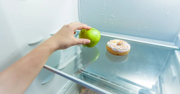 Hand nimmt Apfel statt Donut liegt im Kühlschrank — Stockfoto