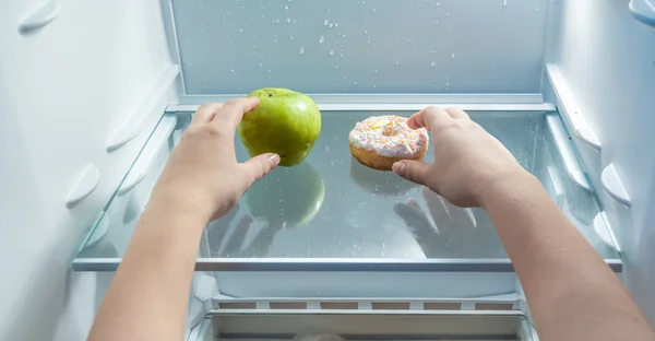Руки с зеленым яблоком и пончиком из холодильника — стоковое фото