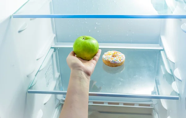 Women hand holding apple instead of donut in refrigerator — Stock Photo, Image