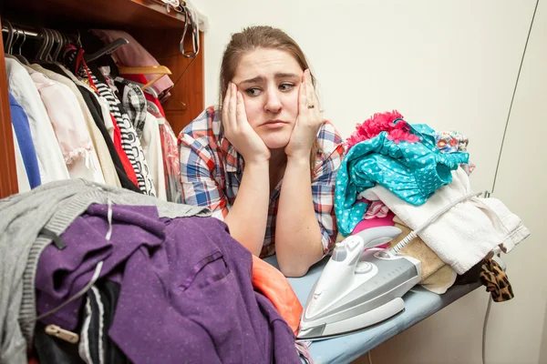 Sad woman leaning against huge pile of not ironed clothes — Stock Photo, Image