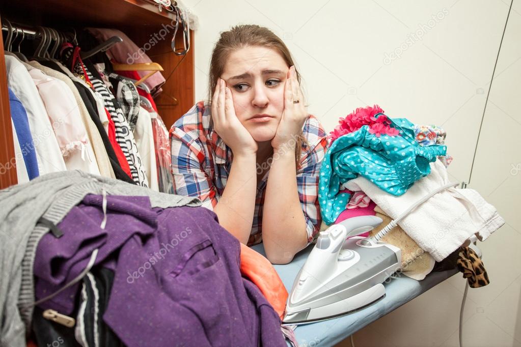 Sad woman leaning against huge pile of not ironed clothes