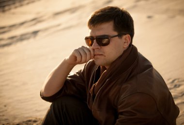 Kumul üzerinde oturan güneş gözlüğü yakışıklı bir adam portresi