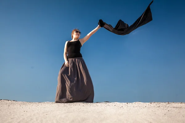 Donna in abito lungo con stoffa nera in piedi su dune di sabbia — Foto Stock