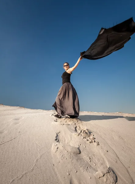 Woman in long dress holding long cloth on sand dune — Stock Photo, Image
