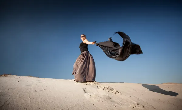 Mulher com pano preto andando sobre dunas de areia — Fotografia de Stock