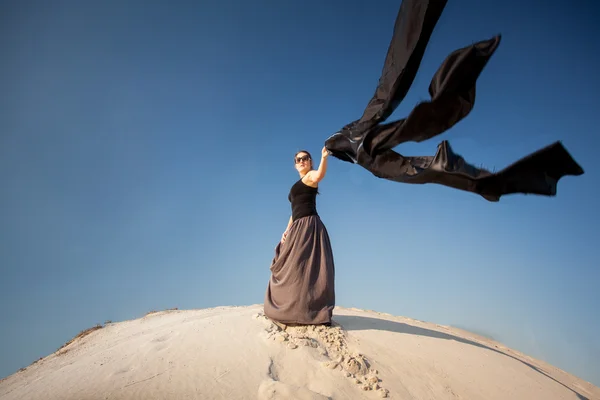 바람이 부는 날에 모래 언덕에 검은 천을 들고 여자 — 스톡 사진