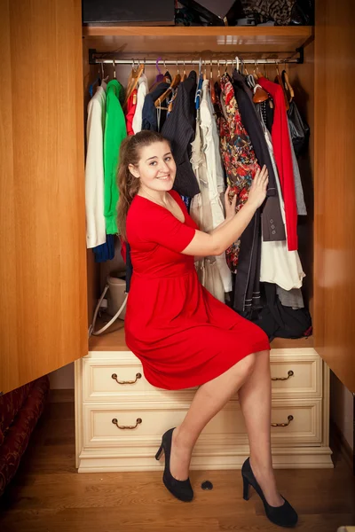 Beautiful woman in red dress sitting at big wardrobe — Stock Photo, Image