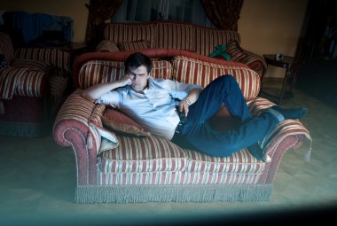 man lying on sofa and watching TV at night clipart