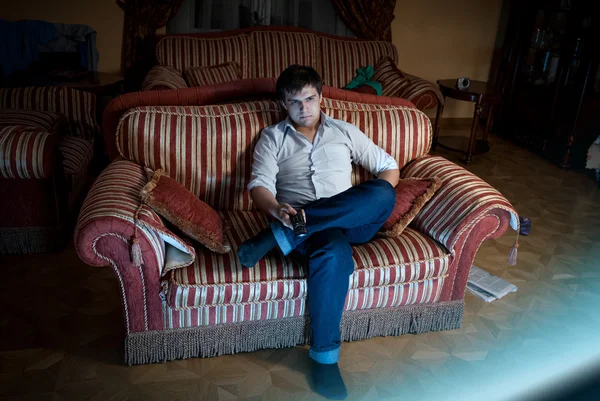 Чоловік перемикає телевізійні канали, сидячи на дивані — стокове фото