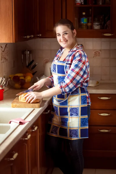 Wanita tersenyum memotong roti di papan potong kayu — Stok Foto