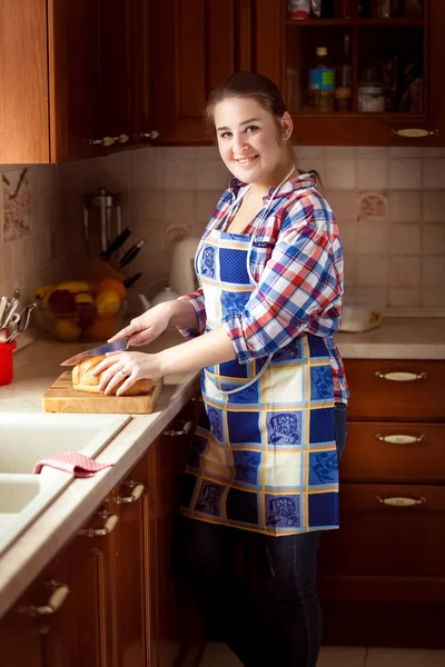 Lächelnde Frau schneidet Brot auf Holzschneidebrett — Stockfoto