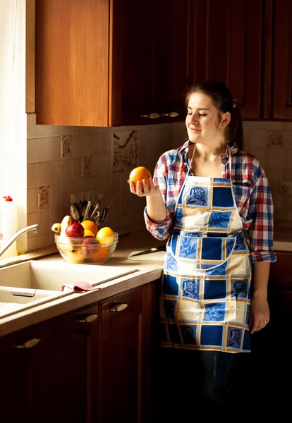 Домохозяйка смотрит на апельсин на деревенской кухне — стоковое фото