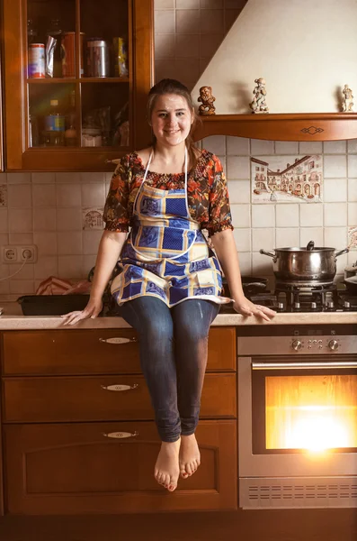 Wanita tersenyum duduk di atas meja sambil memanggang dalam oven — Stok Foto