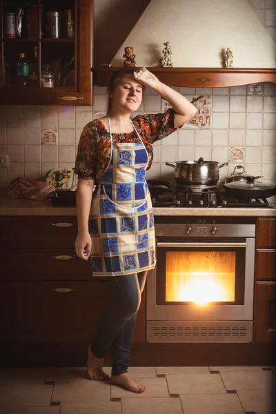 Уставшая домохозяйка, стоящая рядом с рабочей духовкой — стоковое фото