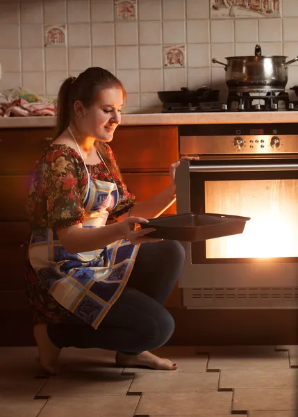 Housewife sitting next to oven and holding pan near hot oven — Stock Photo, Image