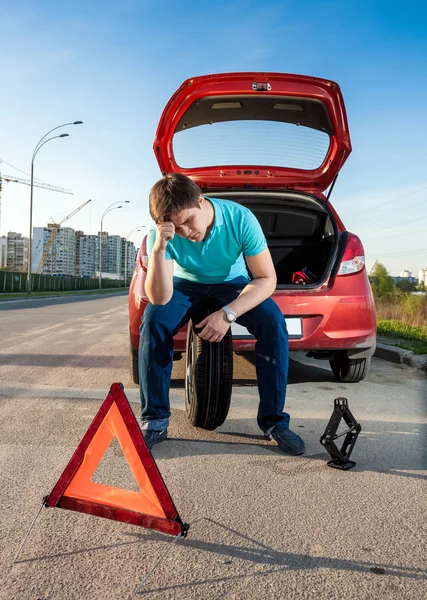 Hombre sentado en la rueda de repuesto cerca de coche roto — Foto de Stock