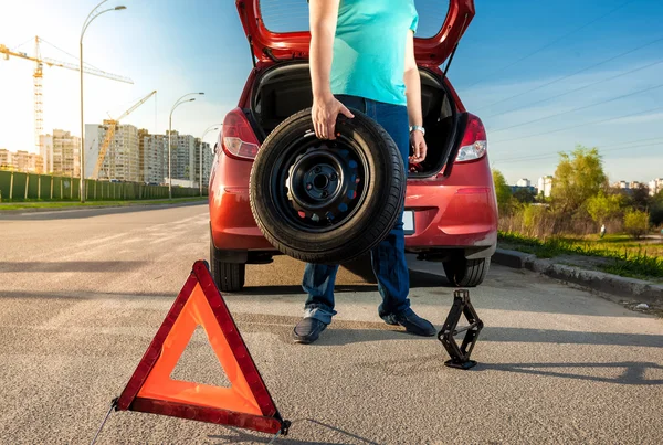 Hombre sosteniendo rueda de repuesto contra coche roto — Foto de Stock